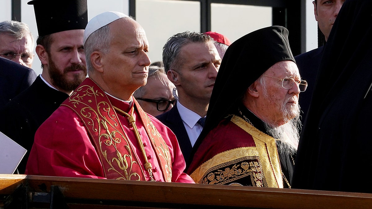 Senior Christian clerics in ornate vestments sit together during an outdoor ceremony.