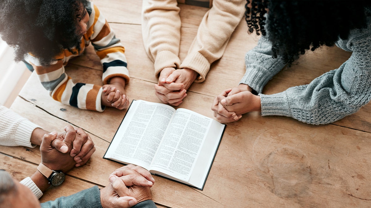 Family with clasped hands around a Bible