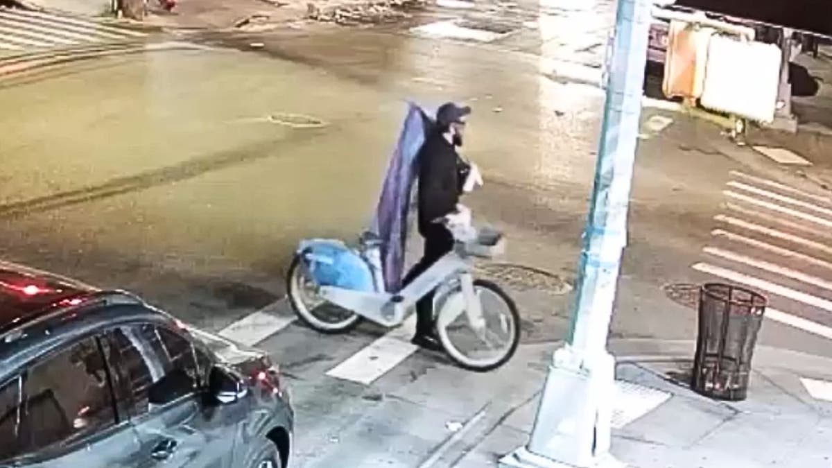 Surveillance image shows a suspect carrying a rainbow flag while riding a bicycle, wanted for defacing three Queens churches with anti-Christian graffiti, police said.