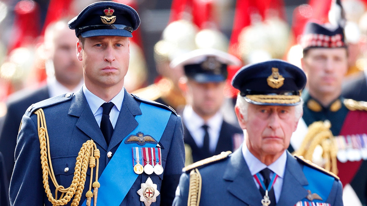 Prince William in military uniform walking behind his father King Charles also in military uniform.