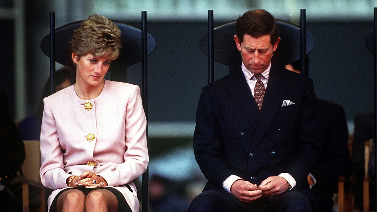 Princess Diana and Prince Charles sitting next to each other looking disappointed.