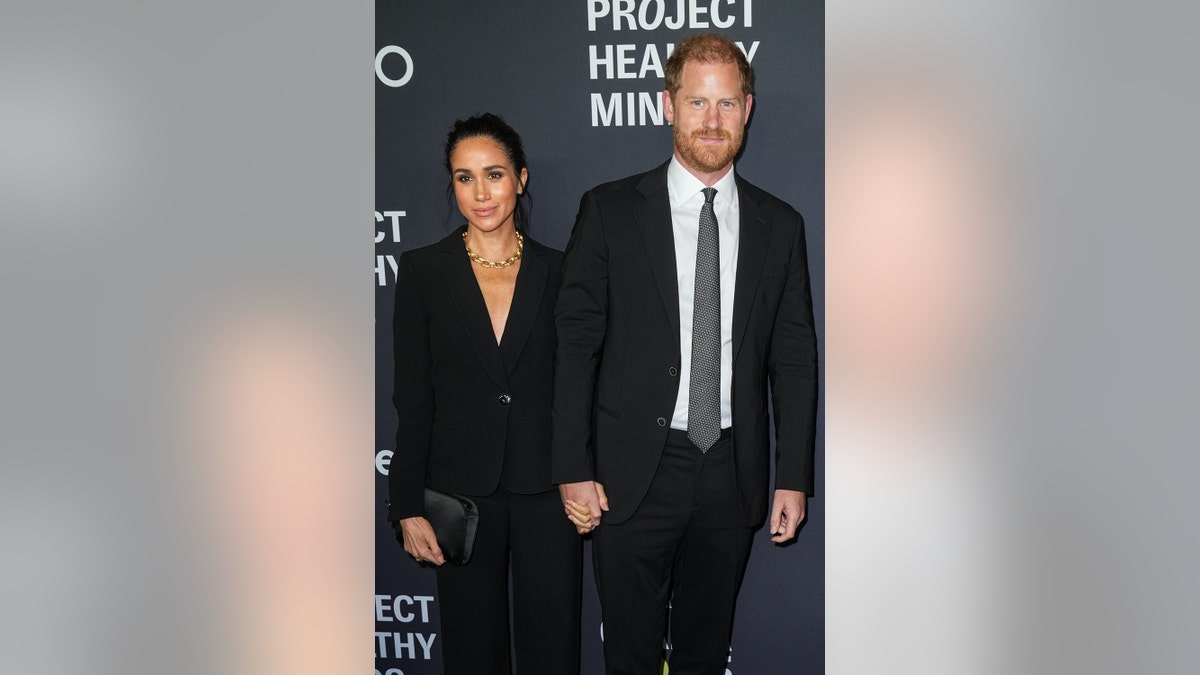 Prince Harry and Meghan Markle standing side-by-side in dark matching attire in New York City.