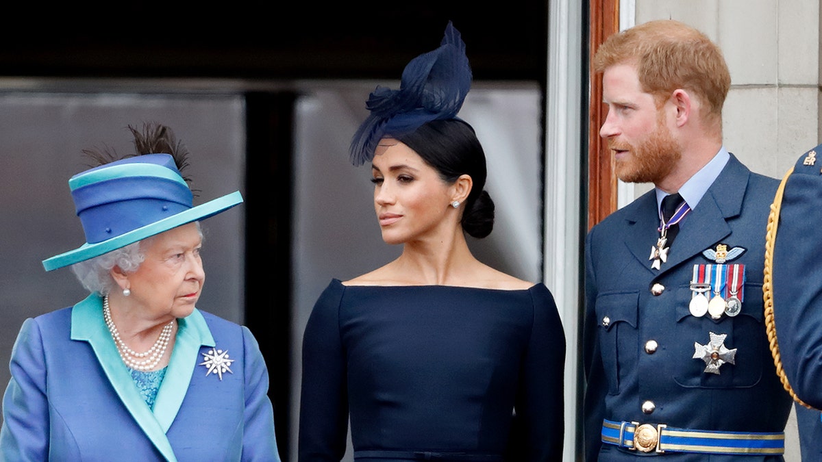 Meghan Markle and Prince Harry looking at Queen Elizabeth II on the palace balcony.