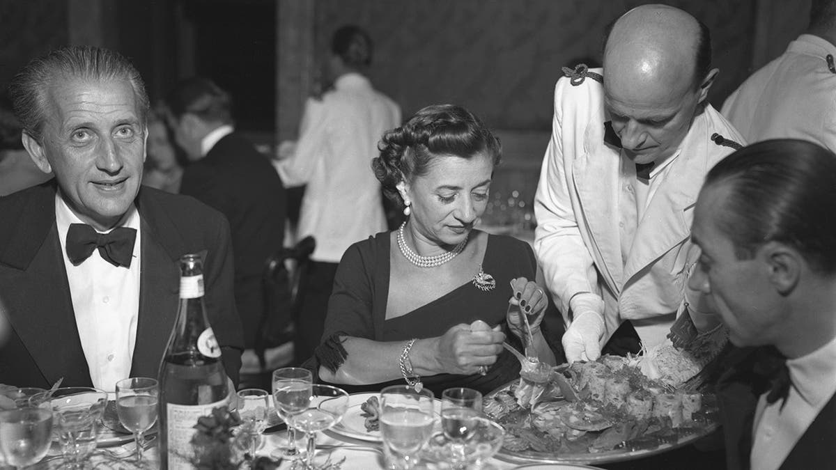Woman serves herself aspic dish from server's tray at fancy dinner event in italy.