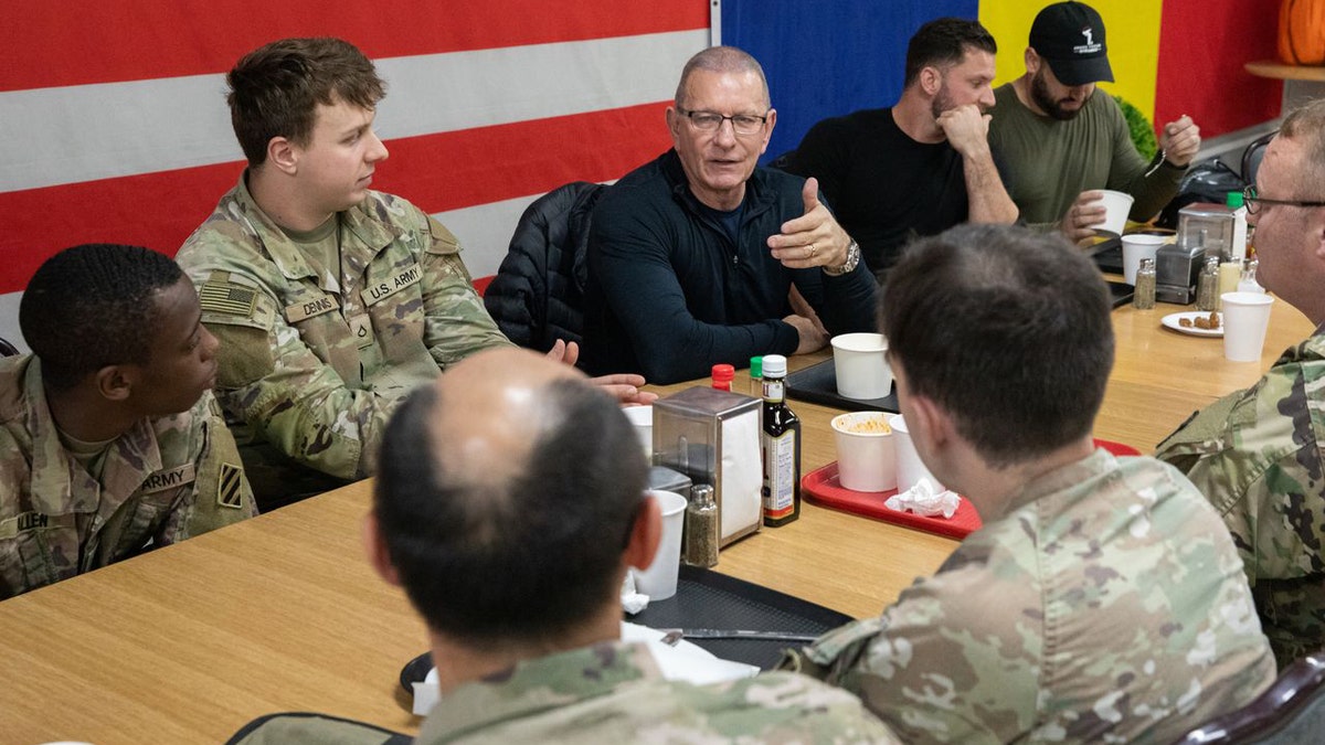 Soldiers sit around a dining table having a conversation during a meal inside a military dining facility.