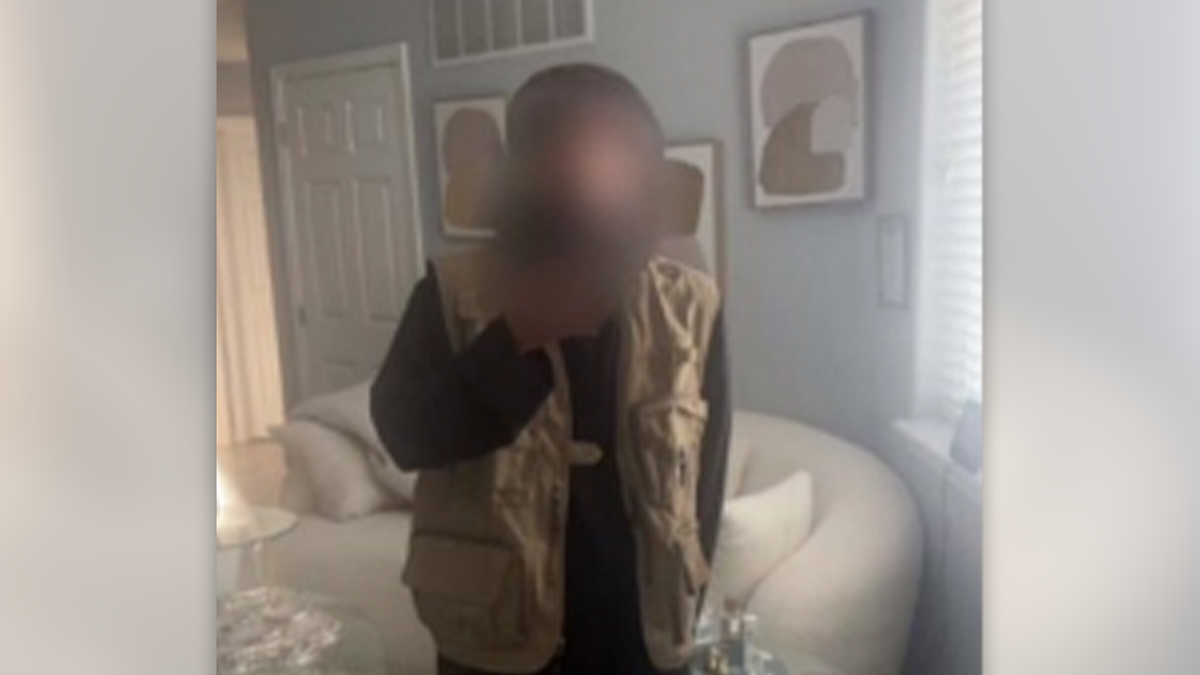 An image of a man whose face has been blurred, taking a selfie while wearing ISIS-style clothing in front of a mirror