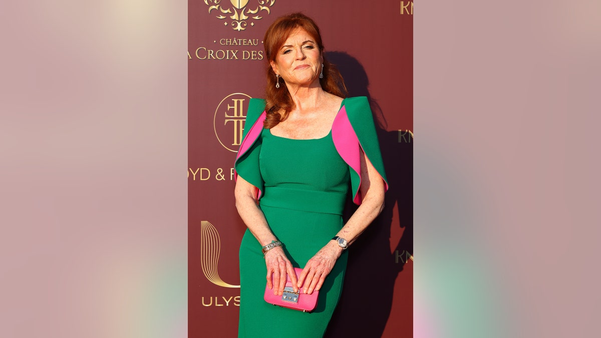 Sarah Ferguson smirking on the red carpet wearing a green and hot pink dress.