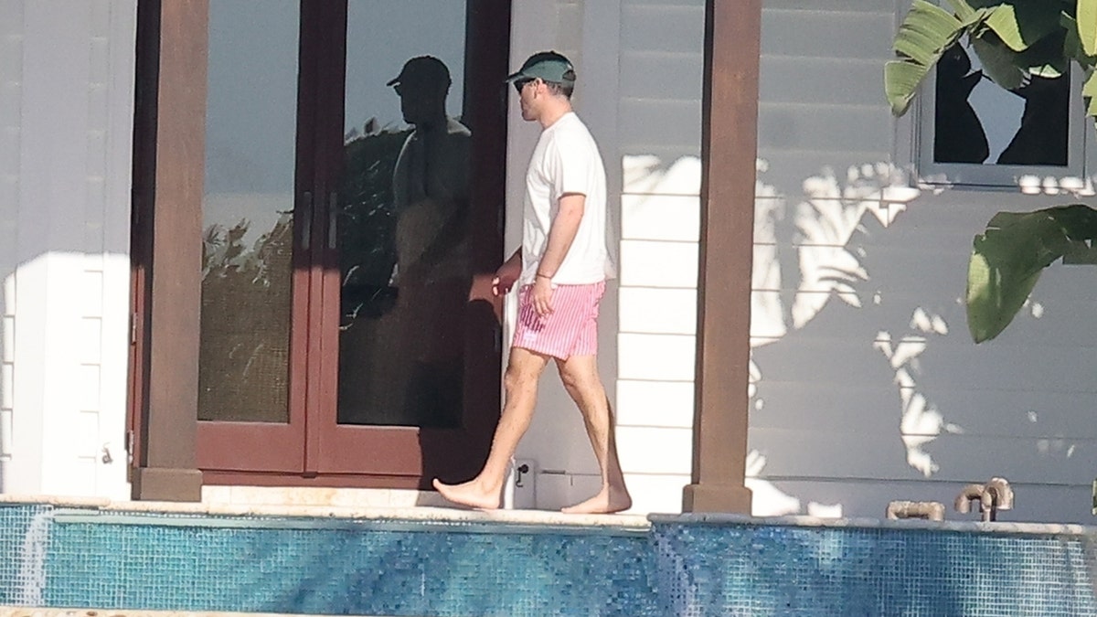 Music executive Scooter Braun is seen barefoot in pink swim trunks and a white shirt, walking by a patio door at Sydney Sweeney’s Florida Keys property.