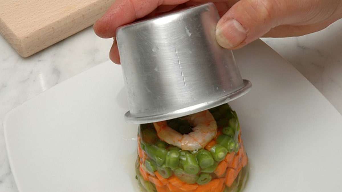 Hand placing small shrimp and vegetable aspic on plate.