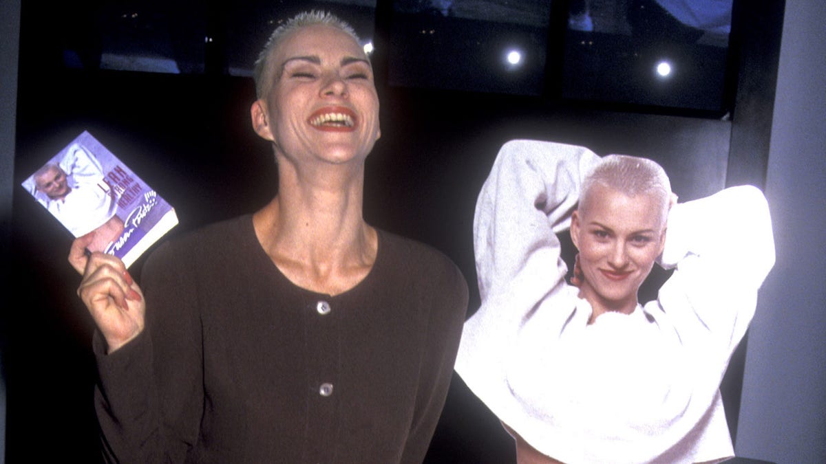 Susan Powter standing in front on cardboard cutout of herself in the 90s