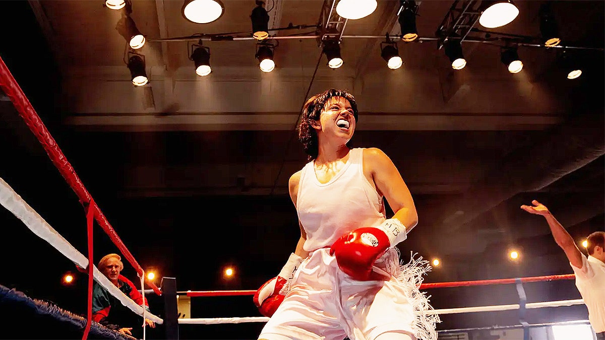Sydney Sweeney portraying boxer Christy Martin in the boxing ring, wearing red gloves and white boxing shorts, mid-match pose.