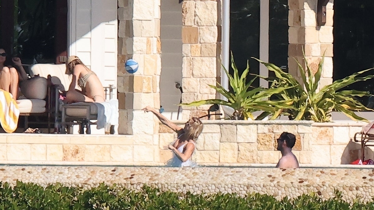 Sydney Sweeney is photographed mid-throw as she tosses a blue-and-white beach ball in the pool, with Scooter Braun standing nearby at her Florida Keys home.