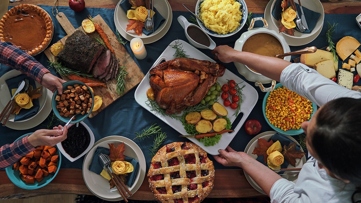 Overhead shot of family sharing Thanksgiving meal, with table full of dishes, sides and desserts.
