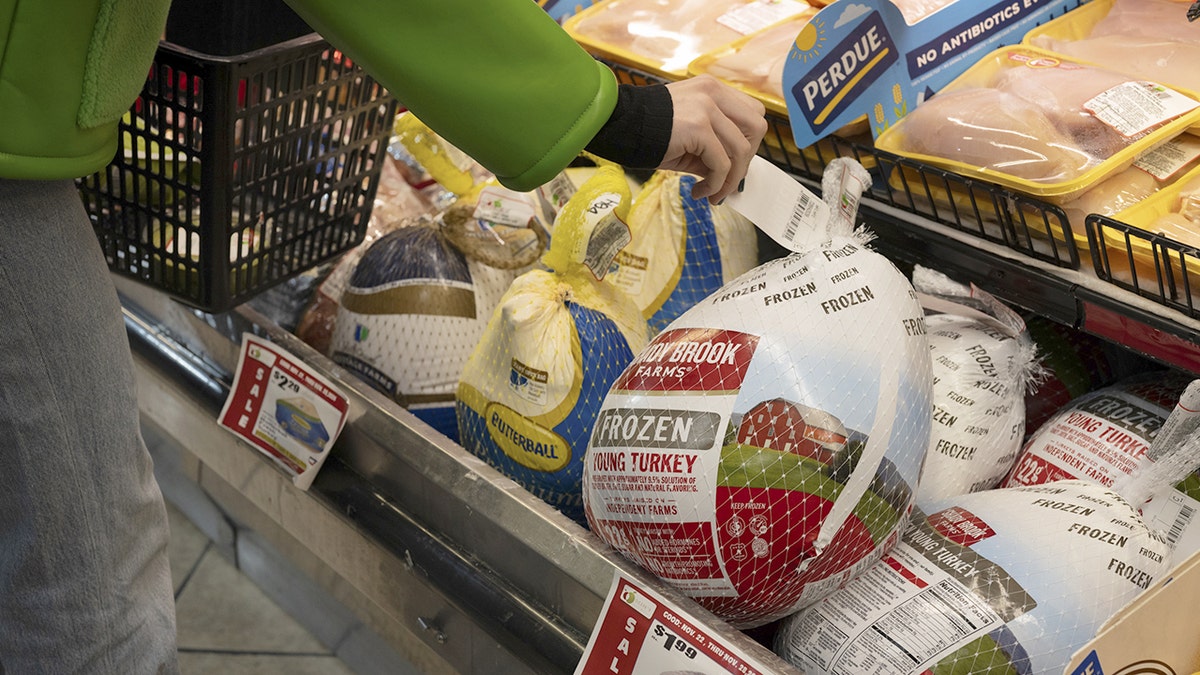 A woman's hand grabs the price tag of a frozen turkey at a supermarket.