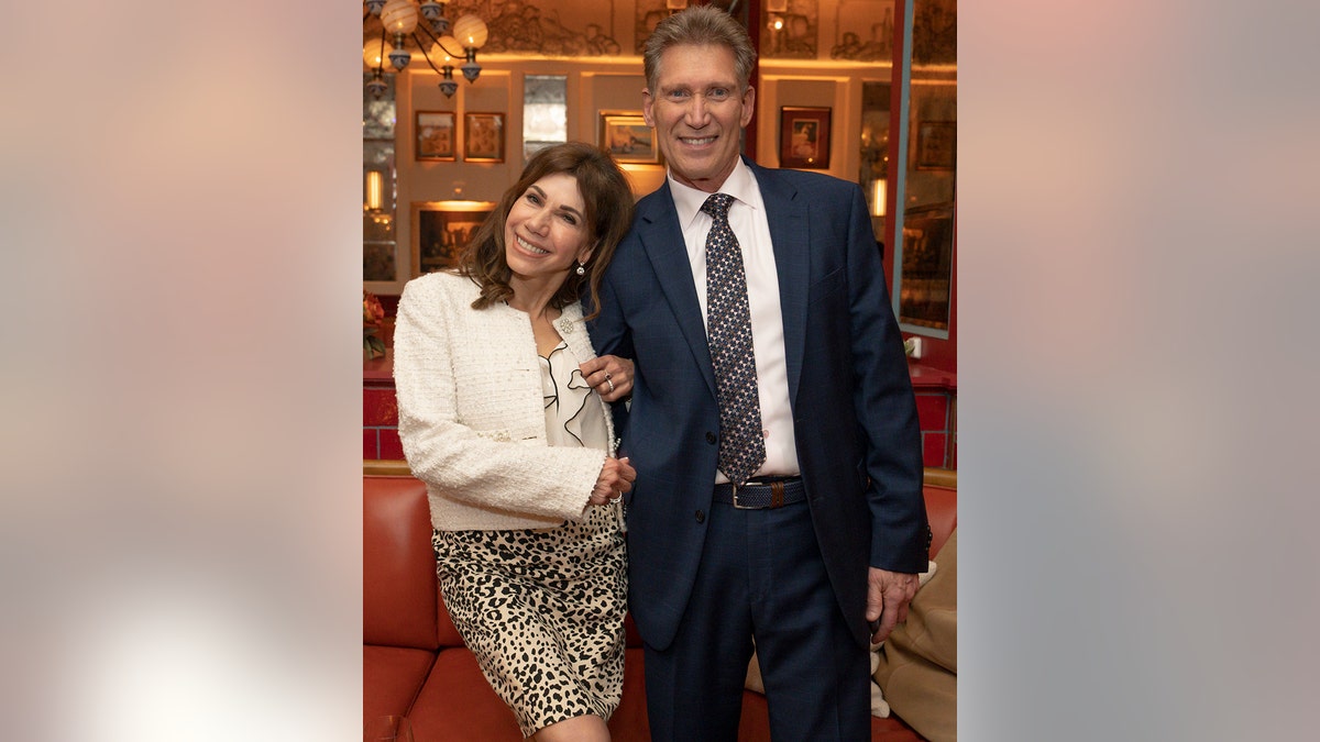 Gerry Turner in a dark blue suit and Theresa Nist in a white sweater with an animal-print skirt as they're both smiling and holding onto each other.