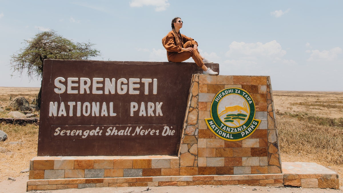 Female traveler sitting on the sign of Serengeti National park, Tanzania