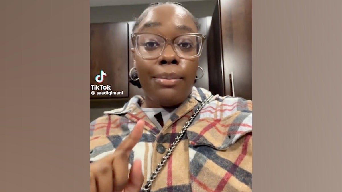 Saadiq Ali speaking in her TikTok video, in kitchen with jacket and purse still on as she gets ready to cook dinner