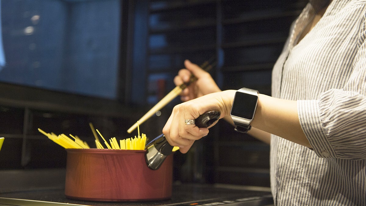 Woman cooking pasta in pot on stove, wearing work blouse in the evening