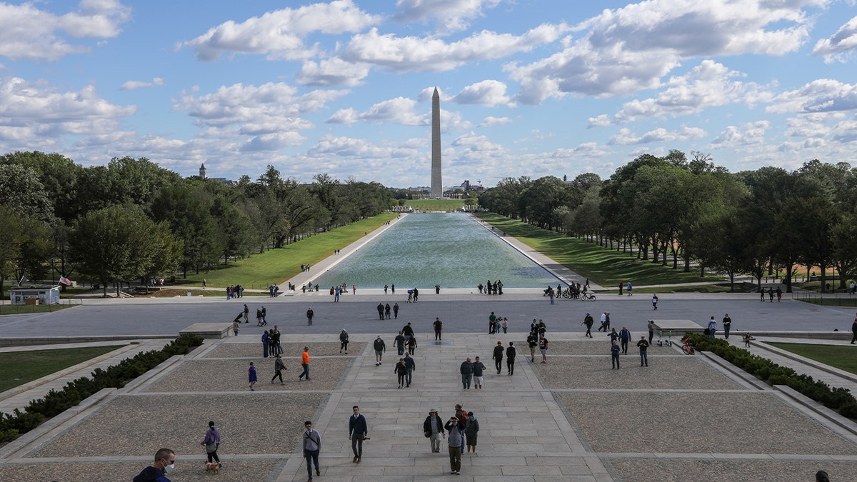 washington monument in back of water pool as tourists visit