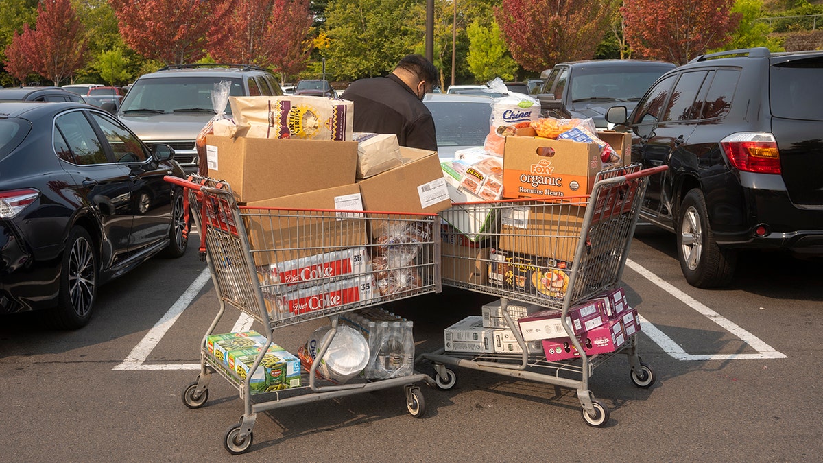 Man seen loading car in parking lot with two carts full of wholesale-size grocery items.