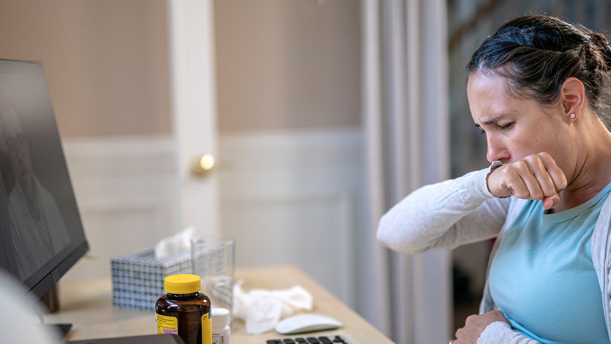 Woman coughing at desk at home