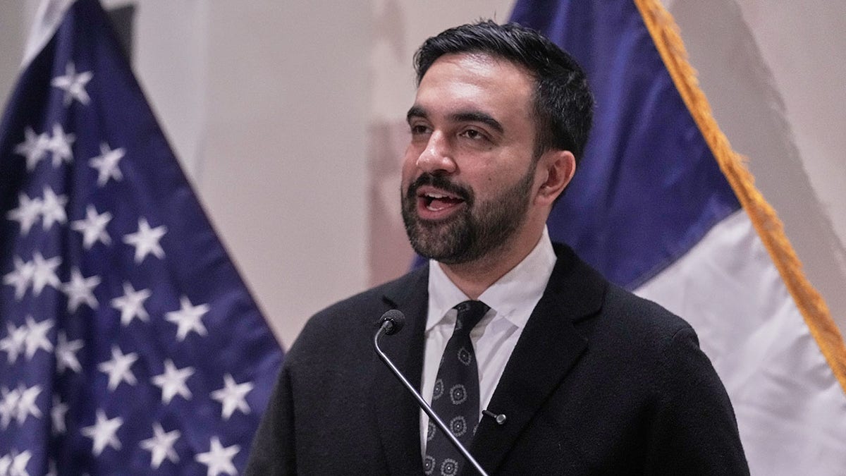 Zohran Mamdani speaking in front of American flag