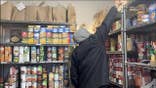 man reaches for a paper bag on a high pantry shelf surrounded by canned goods