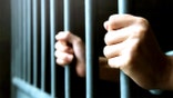 A pair of hands gripping the bars of a jail cell