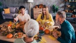 Young adults sit at the Thanksgiving table talking with family members.
