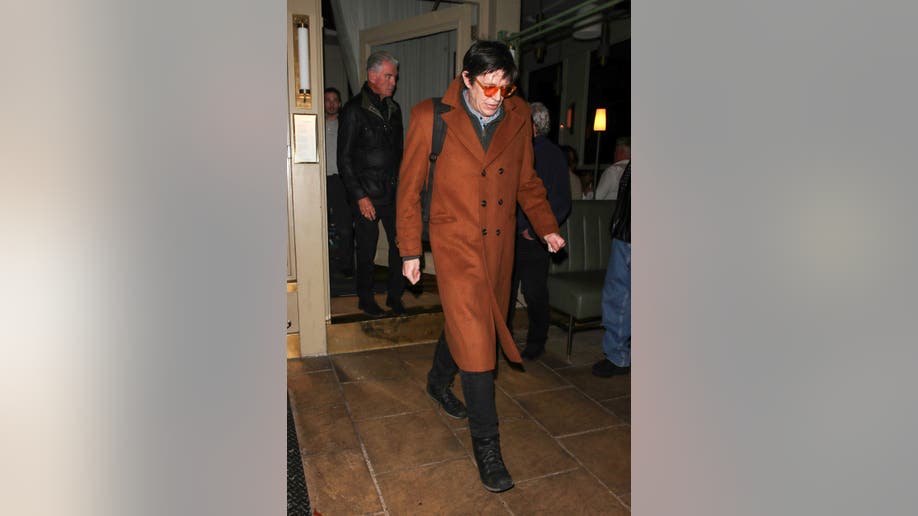 Christopher Brosnan leaves Dorian restaurant in London after a family dinner, wearing an orange overcoat and glasses, followed by his father Pierce Brosnan.