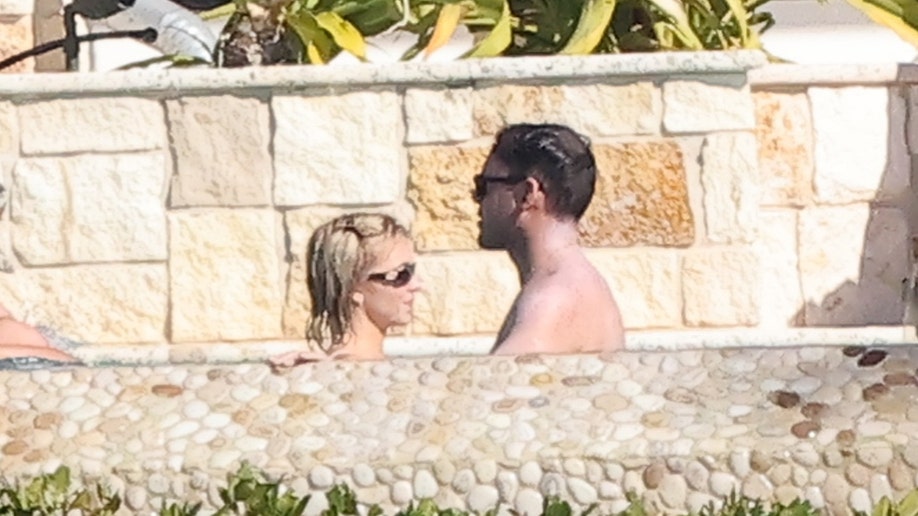 Sydney Sweeney and Scooter Braun are seen standing in the pool, wearing sunglasses and talking near a stone wall at her Florida Keys property.