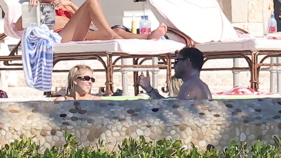 Sydney Sweeney and Scooter Braun are seen talking and smiling while standing in the pool, with lounge chairs and towels visible behind them at her Florida Keys property.