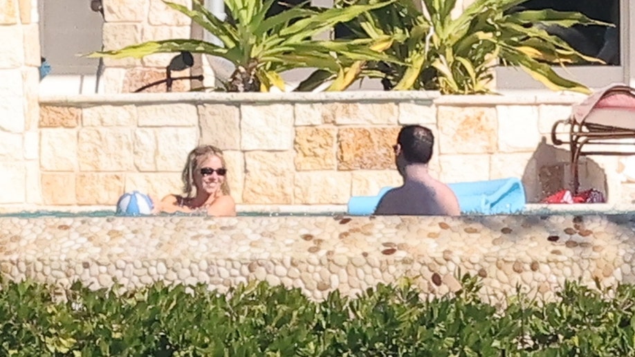 Sydney Sweeney, wearing sunglasses, holds a blue-and-white beach ball while talking with Scooter Braun in the pool at her Florida Keys home.