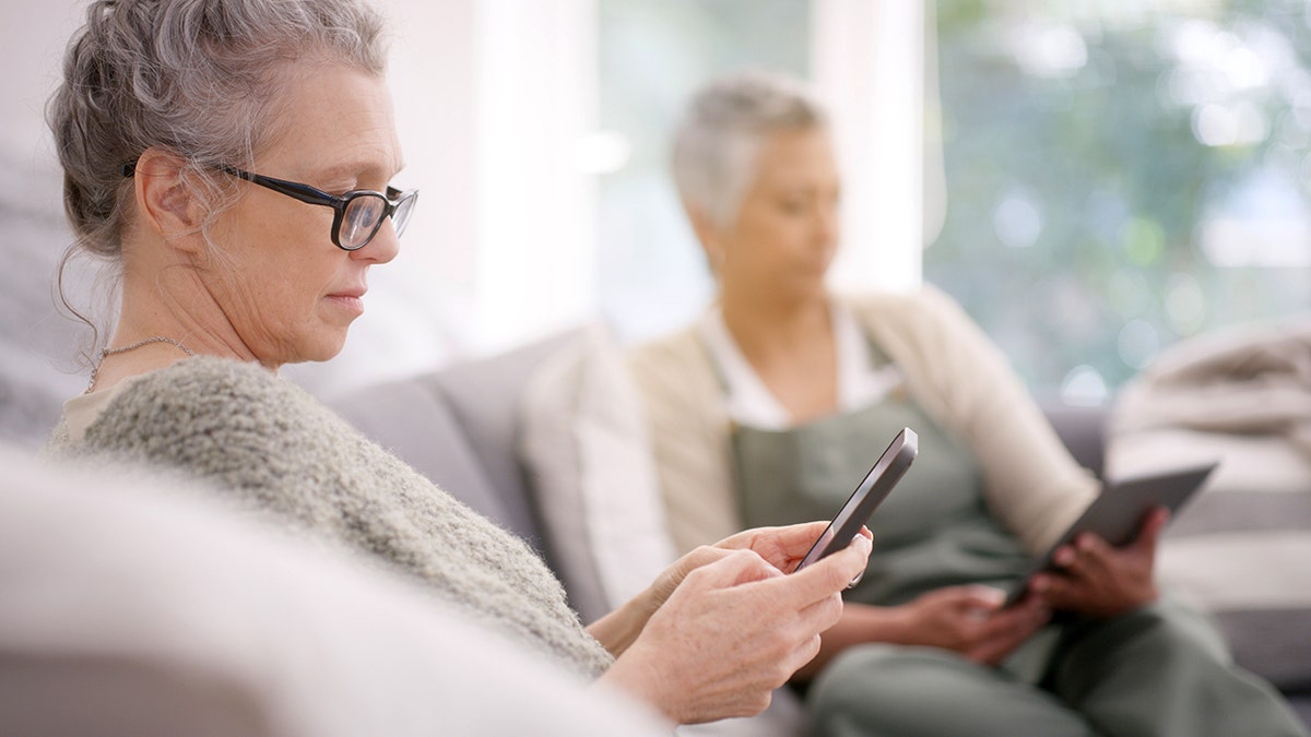 Senior women using smartphone while sitting on sofa in living room