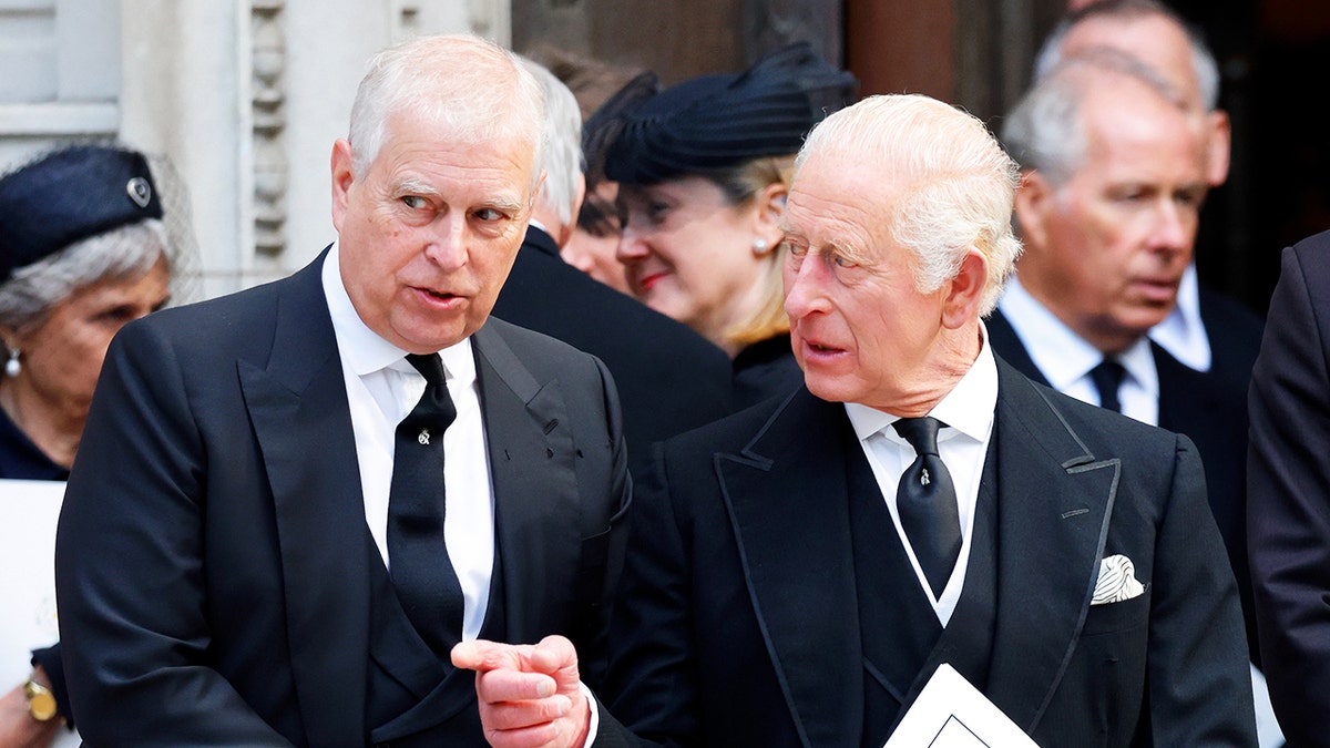 King Charles pointing and having a stern conversation with ex-Prince Andrew as they wear matching black suits.