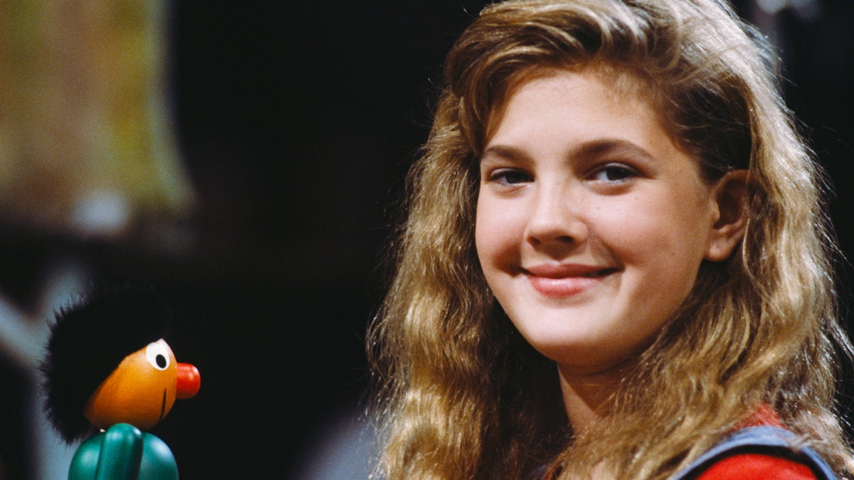 Drew Barrymore smiling next to a puppet.