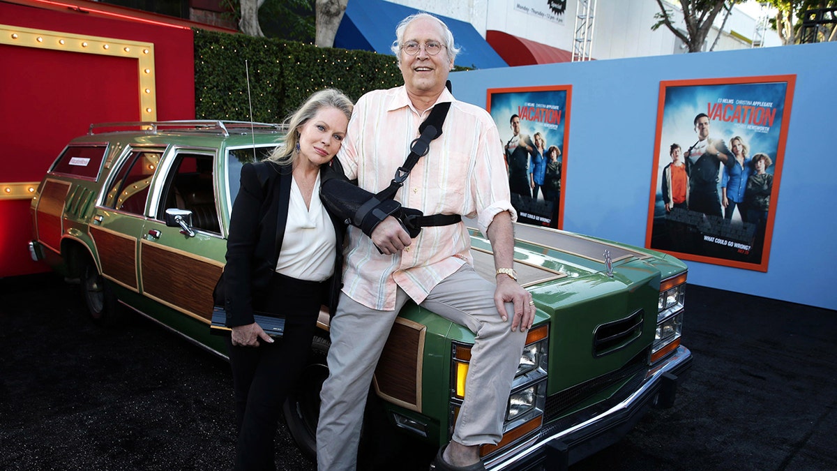 Beverly D'Angelo leaning on Chevy Chase as he sits on a car.