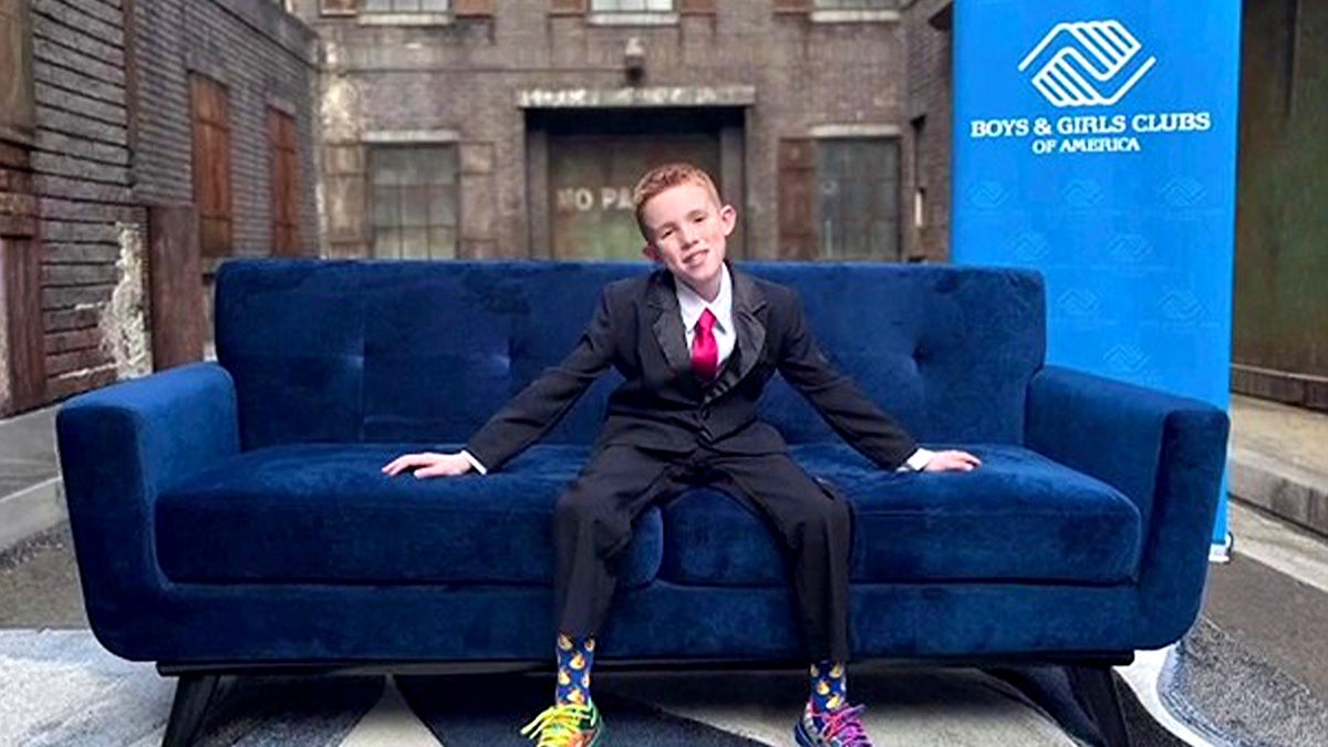 Bex seated on a blue couch with a Boys & Girls Club banner behind him