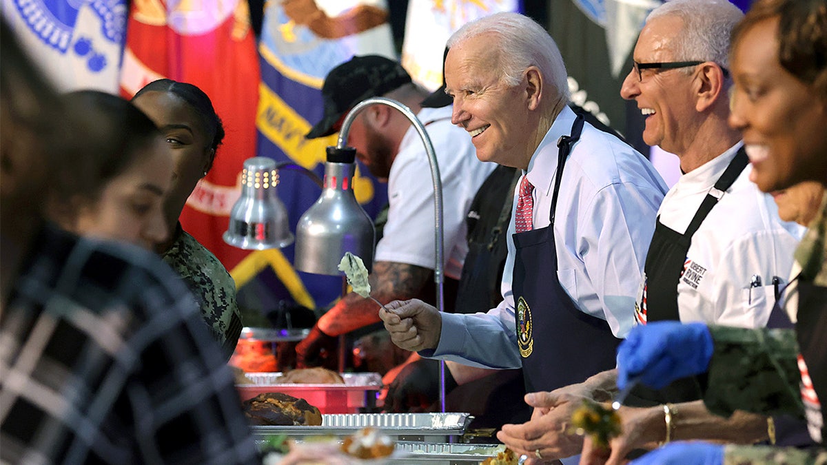 President Joe Biden serves food to service members alongside chef Robert Irvine during a holiday dinner event.