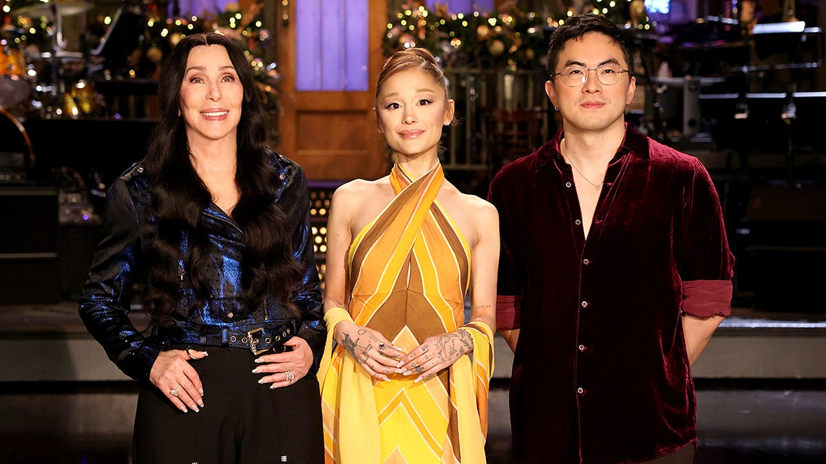 Cher, Ariana Grande, and Bowen Yang stand together while filming promotional segments for 'Saturday Night Live.'