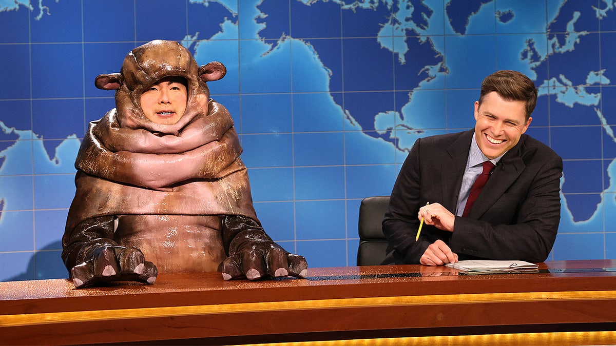 Bowen Yang dressed as Moo Deng the hippo stands beside Colin Jost during a Weekend Update segment.
