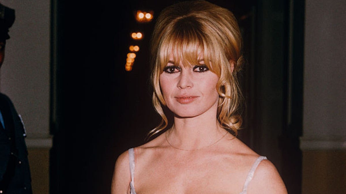Brigitte Bardot stands indoors at the Plaza Hotel in New York, wearing a white evening dress, circa 1970.