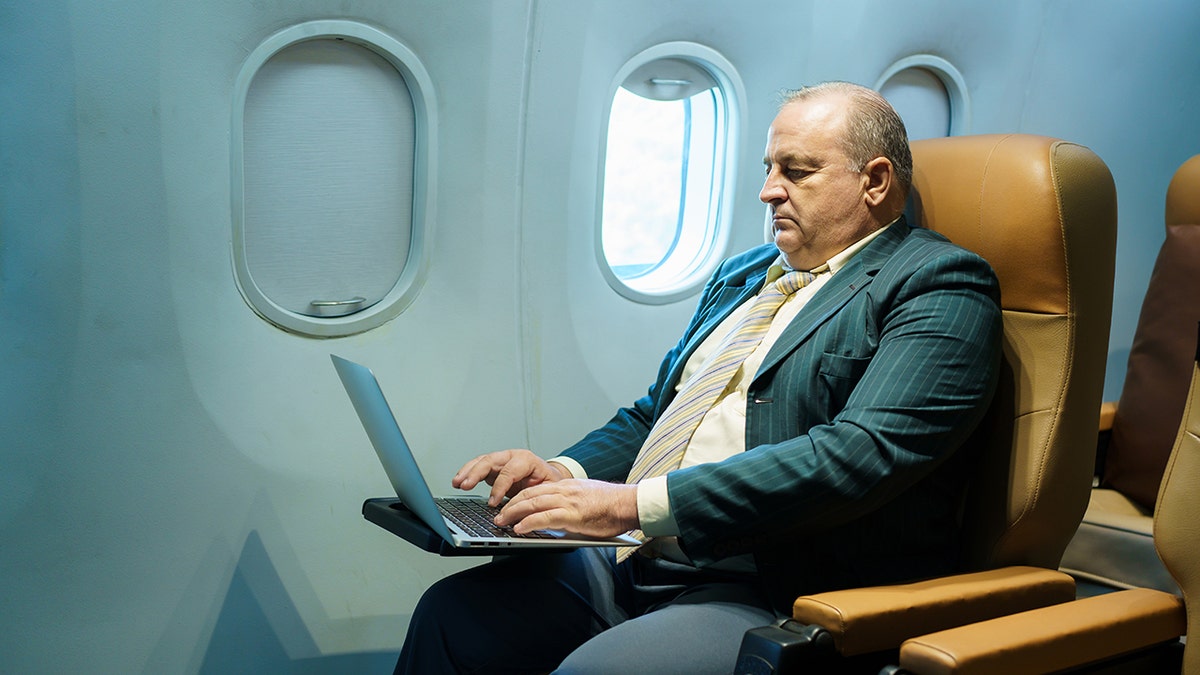 Business traveler working on a laptop while seated in a premium airplane seat during a flight.