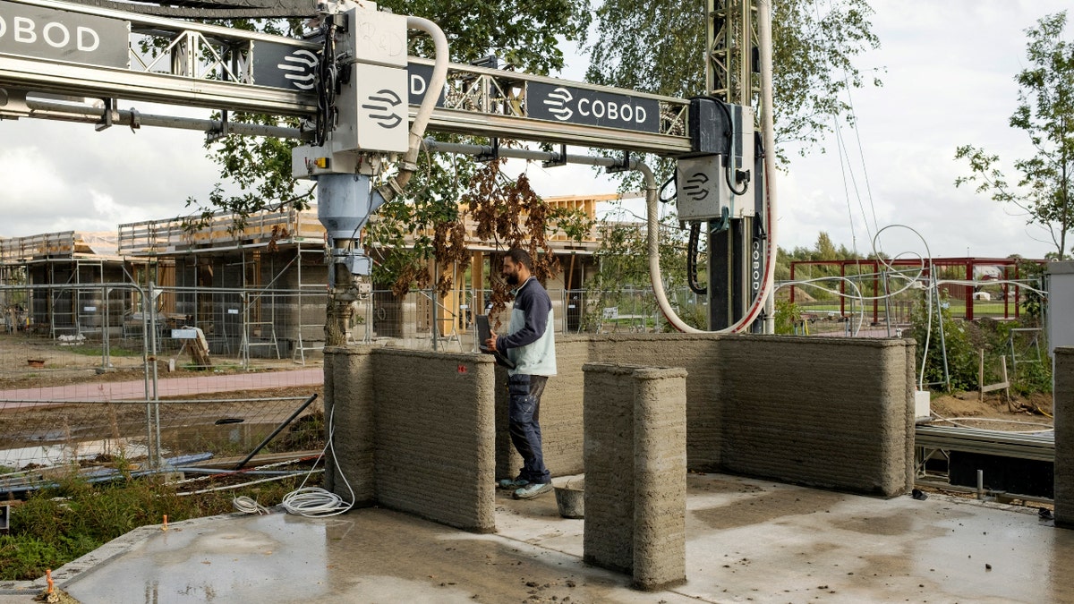 A COBOD BOD3 3D printer extrudes concrete on site to form structural walls for student apartments under construction.
