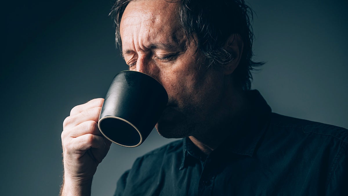 Middle aged man drinking coffee with eyes closed, looking tired or stressed.