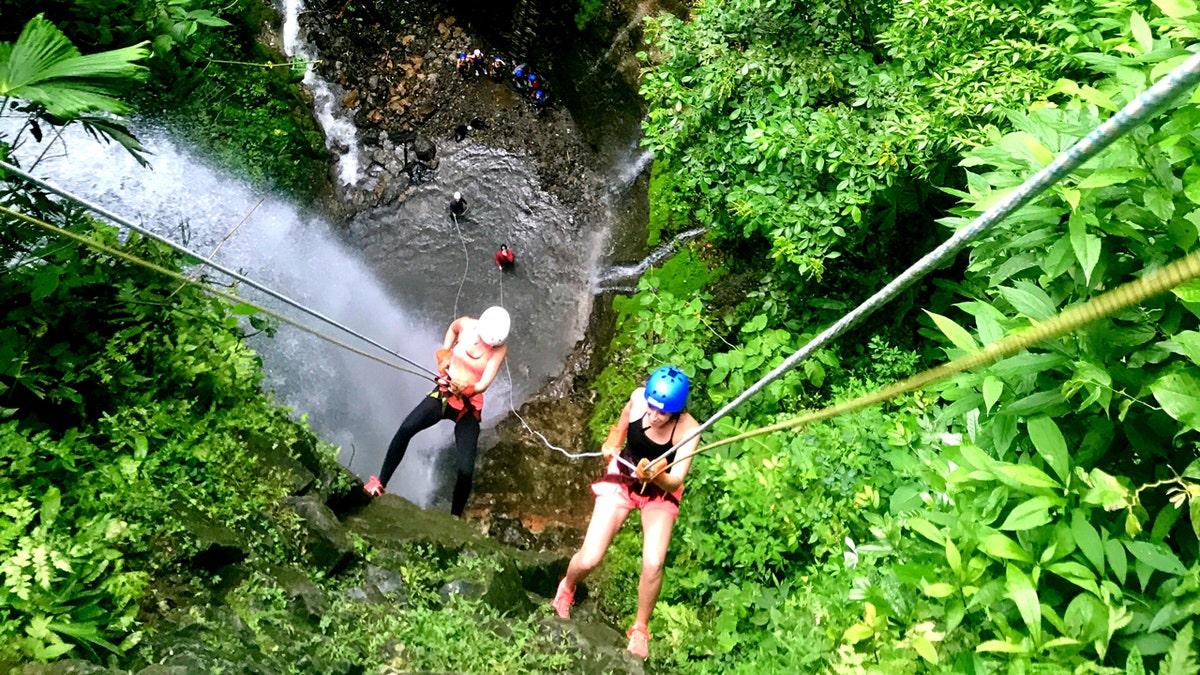 two people rock climbing over waterfall