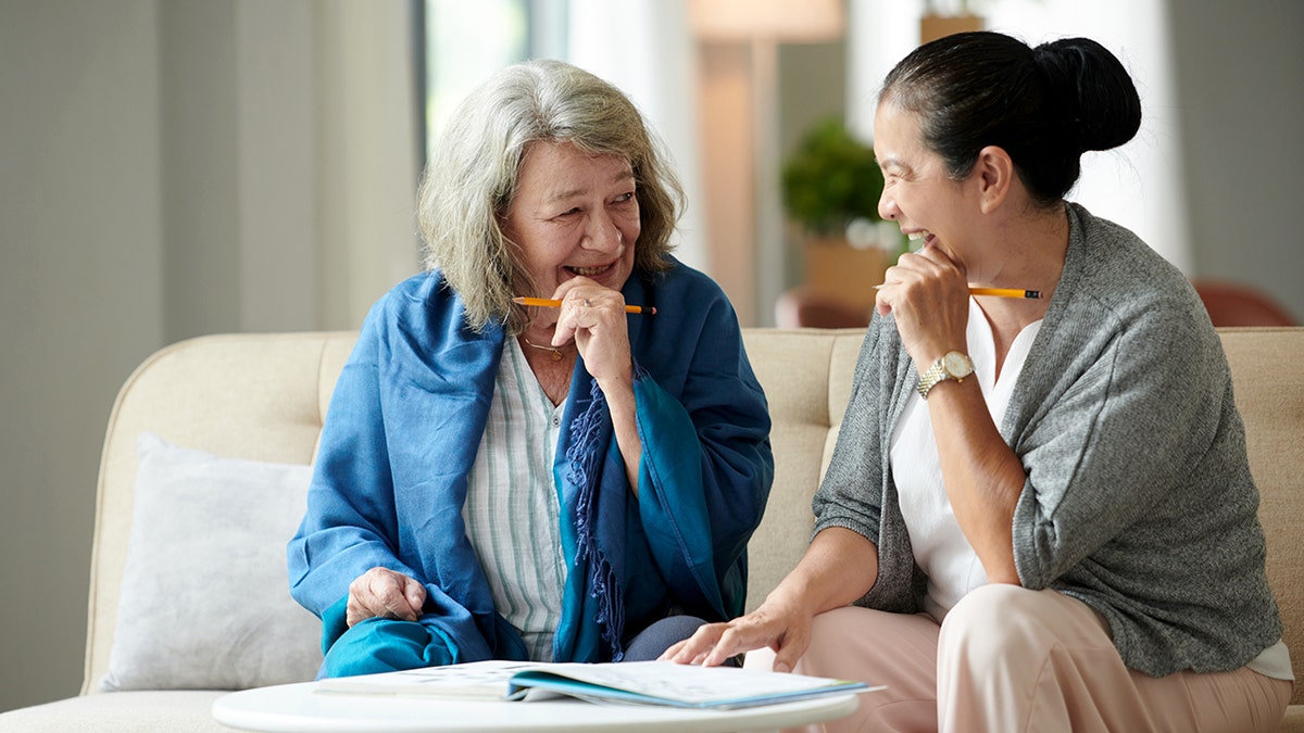 Joyful female friends thinking on answer for crossword puzzle