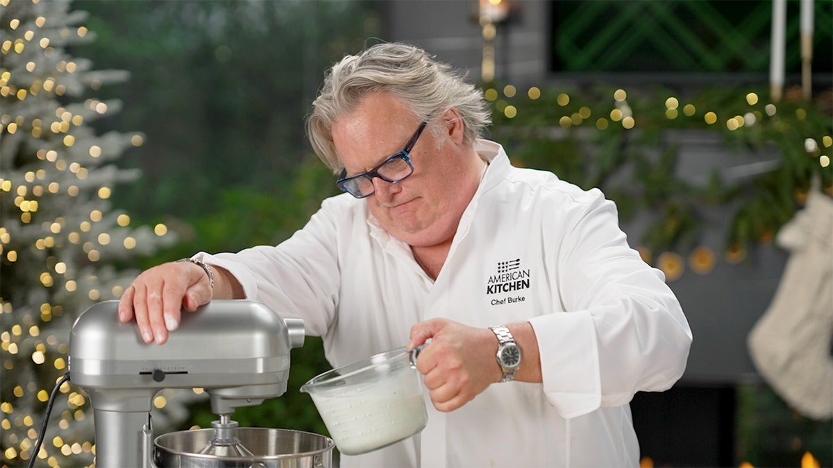 "American Kitchen" chef David Burke prepares to pour ingredients into a mixer against a backdrop of Christmas.
