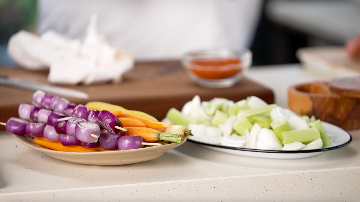 Onions, carrots and celery are shown on plates.