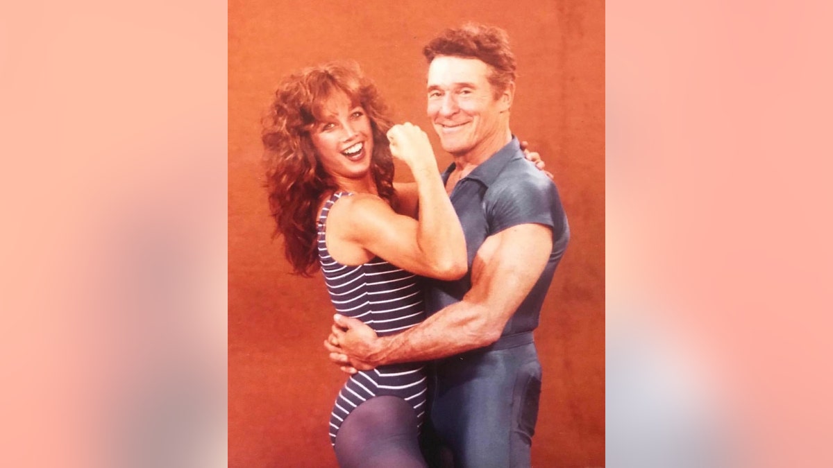 A young Denise Austin in workout gear being held by Jack LaLanne.